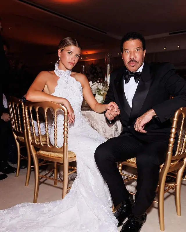 The father-daughter duo holds hand as they sit on the chair for a quick snap