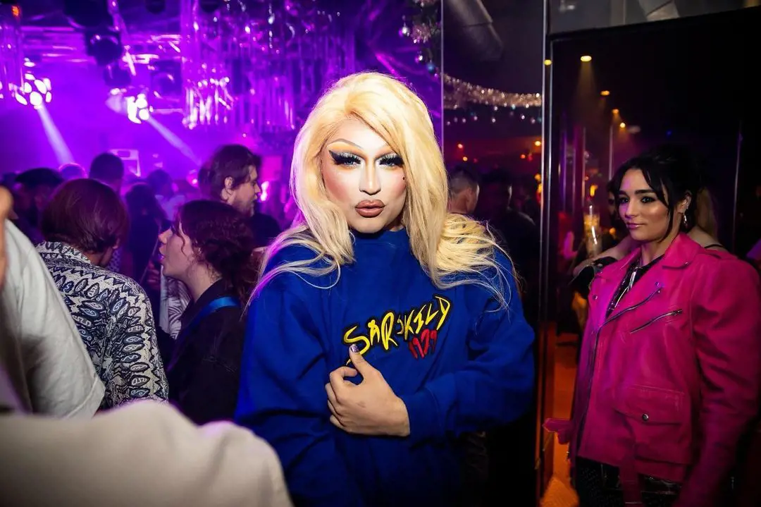 Indiana can be spotted in a pink outfit at the background as her sister Miss Cara poses at Connections Nightclub in December, 2022